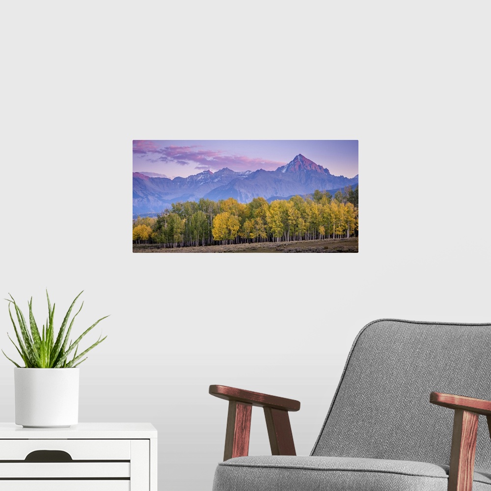 A modern room featuring A photograph of purple mountains seen in the distance with a forest in autumn foliage in the fore...