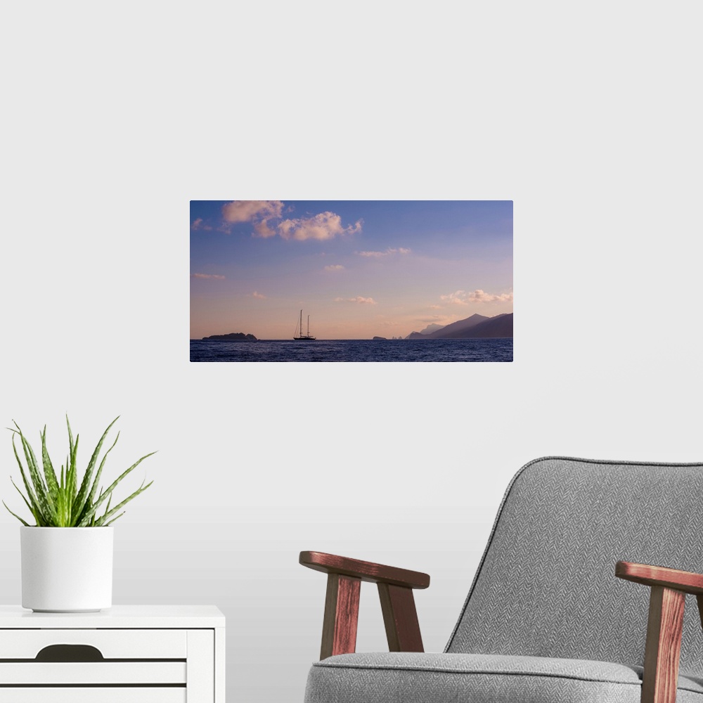 A modern room featuring Photograph of a single sailboat in the middle of the ocean with silhouettes of mountains in the d...