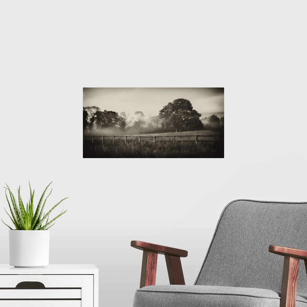 A modern room featuring A horizontal photograph of a country field with a wooden fence and mist over trees in the distance.
