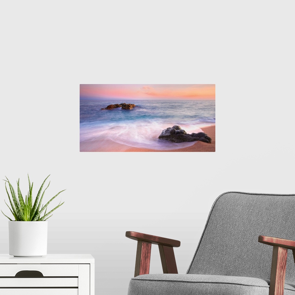 A modern room featuring Panoramic image of gentle waves on a rocky seashore with a vibrant pink sunset.