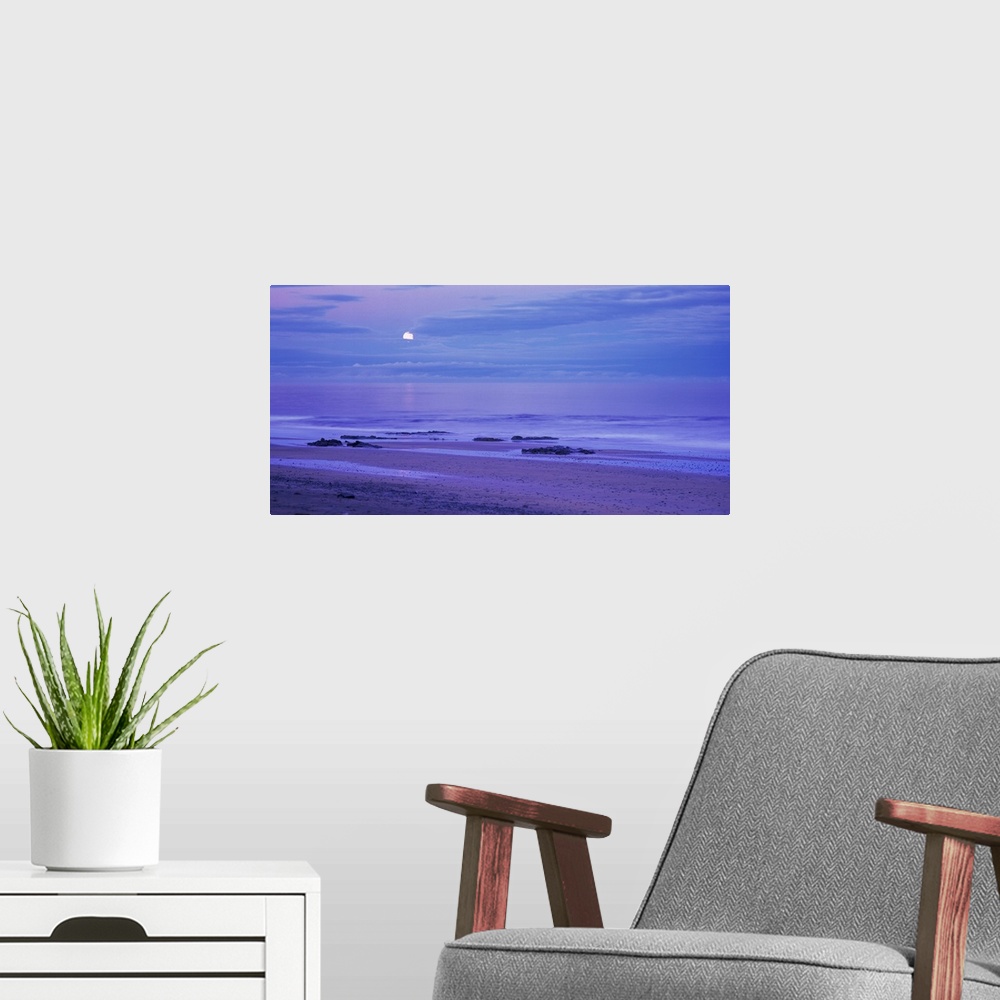 A modern room featuring The moon is seen slightly behind a cluster of clouds that hang over the ocean water and photograp...
