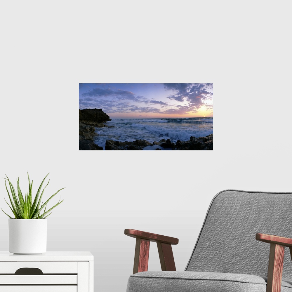 A modern room featuring Oversized artwork of a photograph looking out into the ocean as waves crash onto the rock formati...