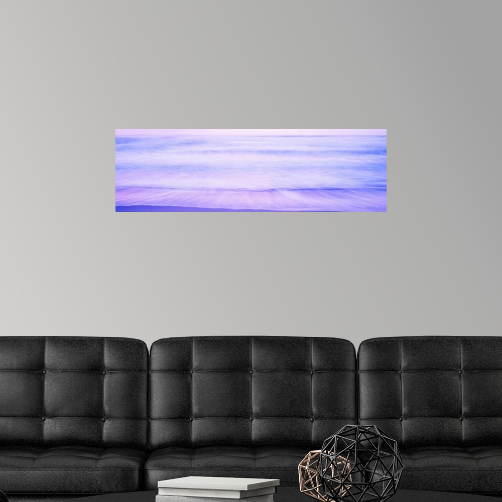 A modern room featuring A large panoramic picture taken of waves that are about to hit the beach with a dusk like sky abo...