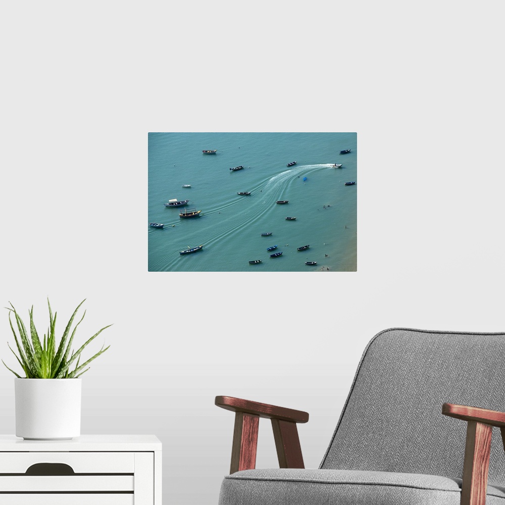 A modern room featuring Aerial photograph of boats anchored on a teal ocean with wave lines creating movement from one mo...