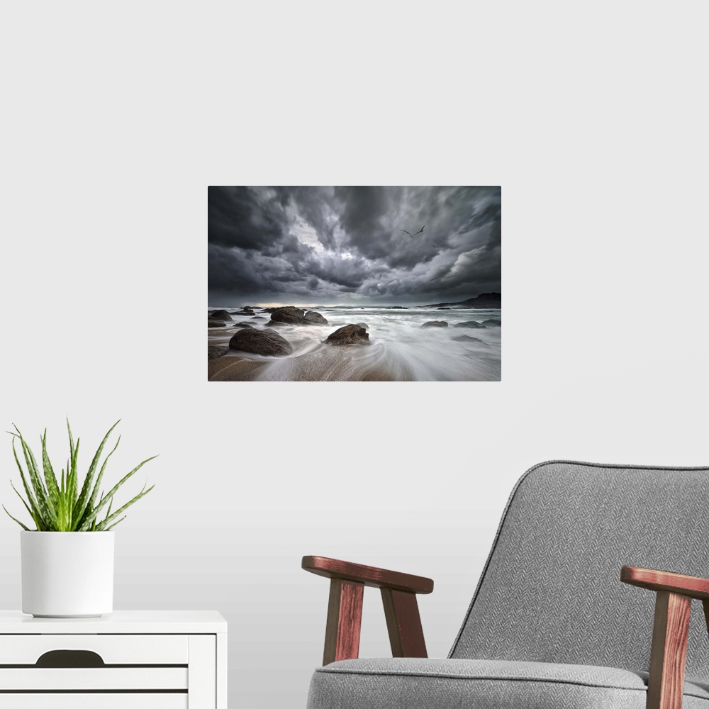A modern room featuring Dramatic clouds hang over a rocky beach with the tide rushing out to sea.