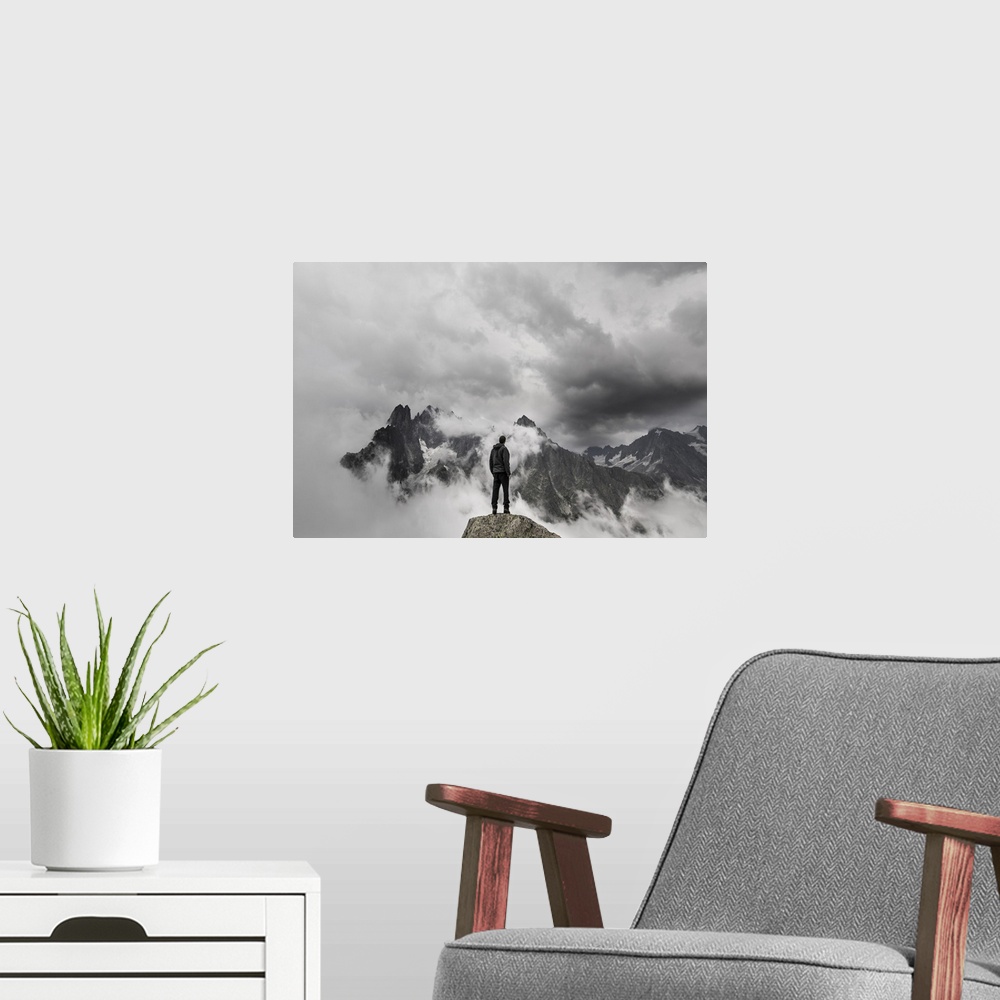A modern room featuring A portrait of a man standing on a large rock formation staring off into the distance at a cloudy ...
