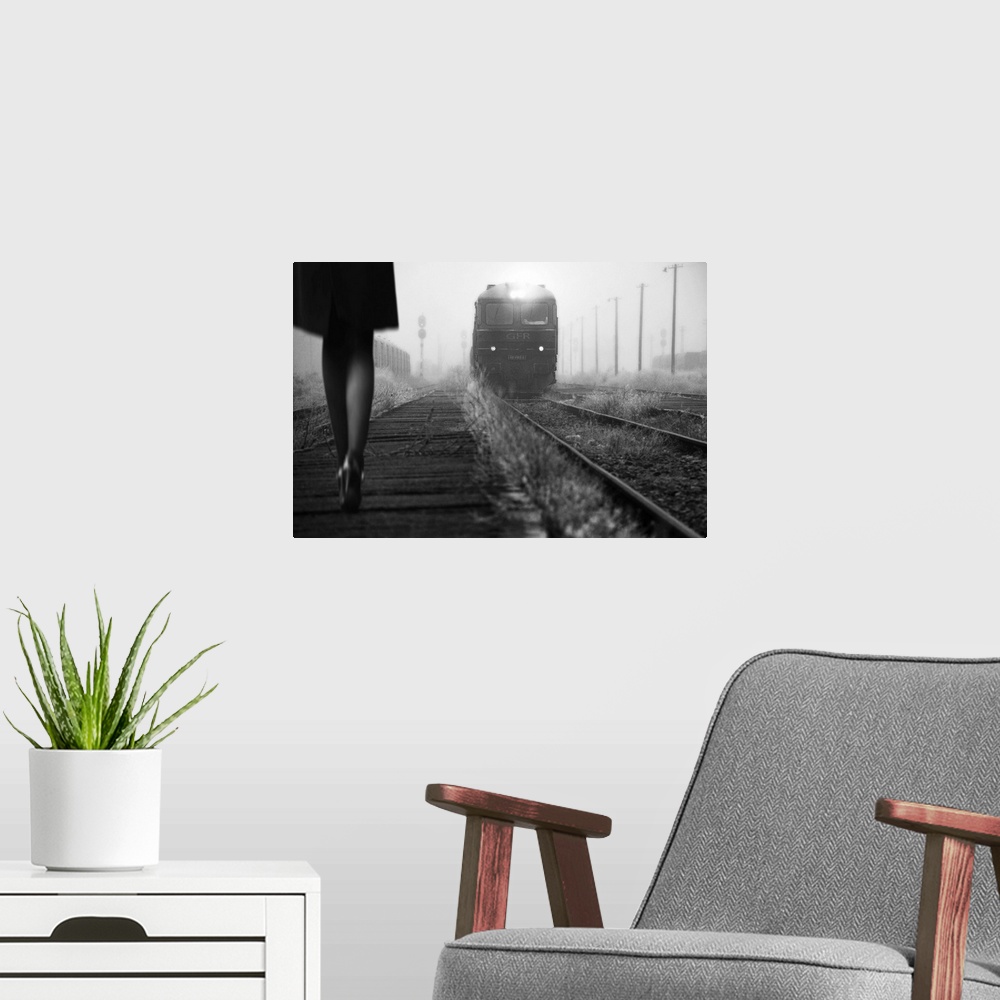 A modern room featuring Black and white image of a woman in heels talking along a path by railroad tracks with an approac...