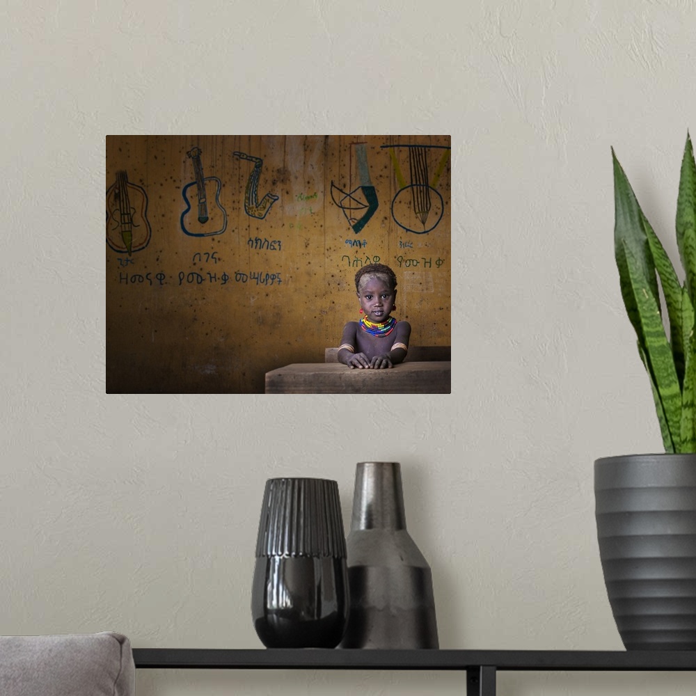 A modern room featuring Portrait of a young child wearing a beaded necklace seated at a desk with drawings of musical ins...