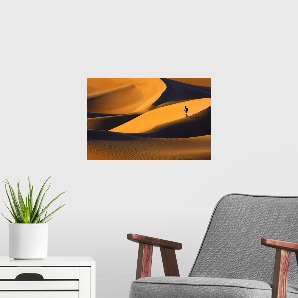 A modern room featuring A person walks on a sand dune in a golden desert at sunset.