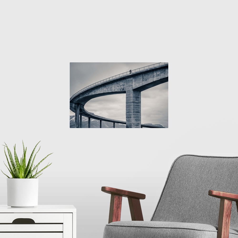 A modern room featuring A biker riding across the top of a tall concrete bridge, Norway.