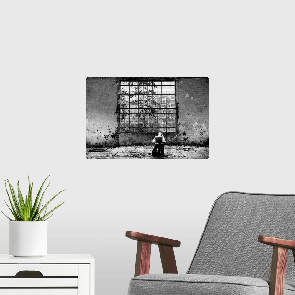 A modern room featuring Conceptual photo of a man sitting at a desk in an abandoned building looking at a laptop.