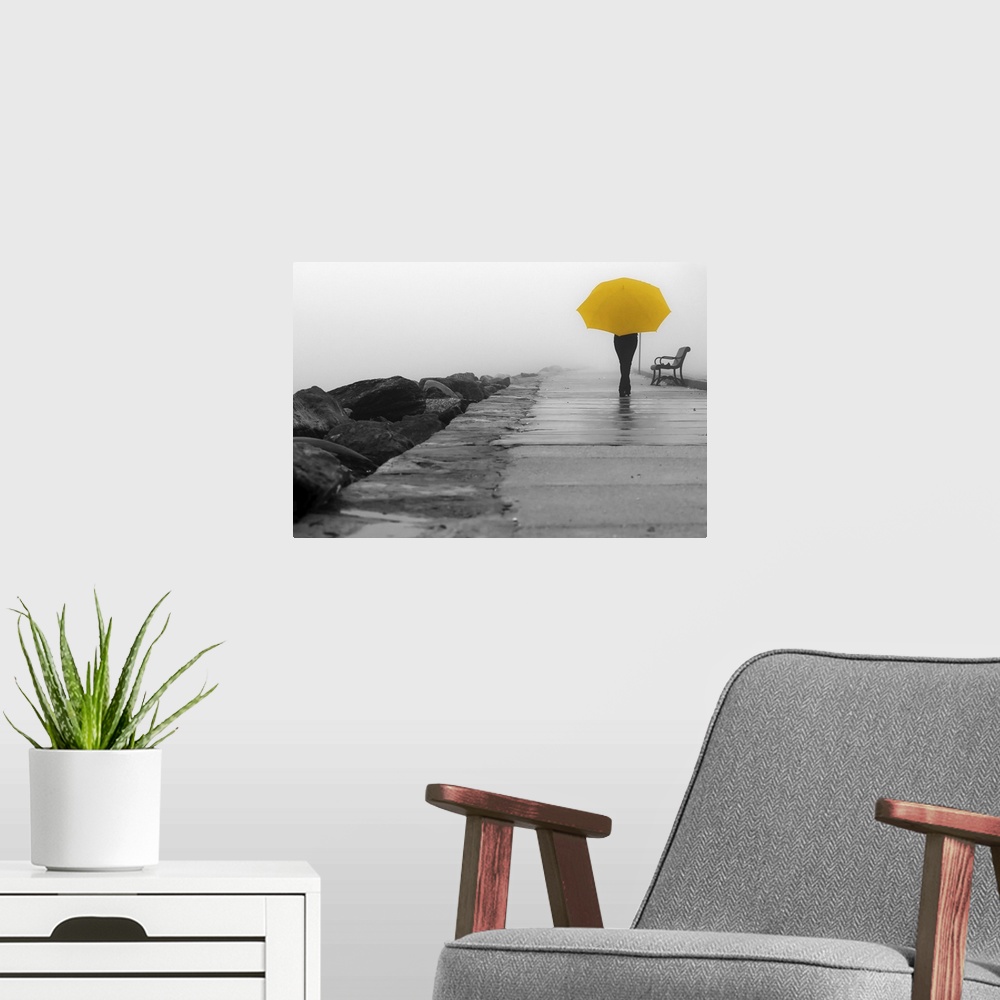 A modern room featuring A black and white photograph of a person with a colorized yellow umbrella sitting on a bench on a...
