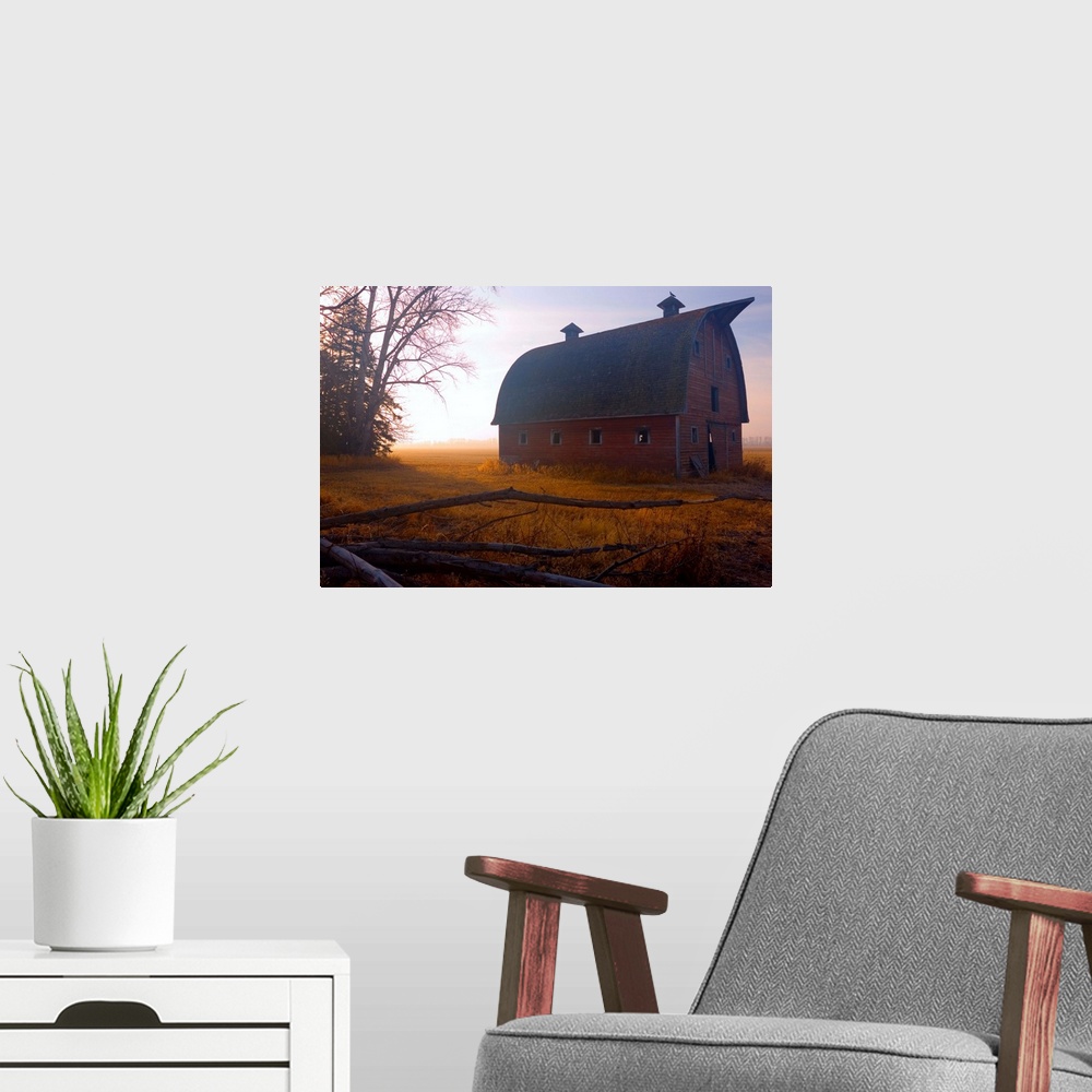 A modern room featuring A large barn is photographed in the morning during sunrise and there is a thin layer of fog over ...