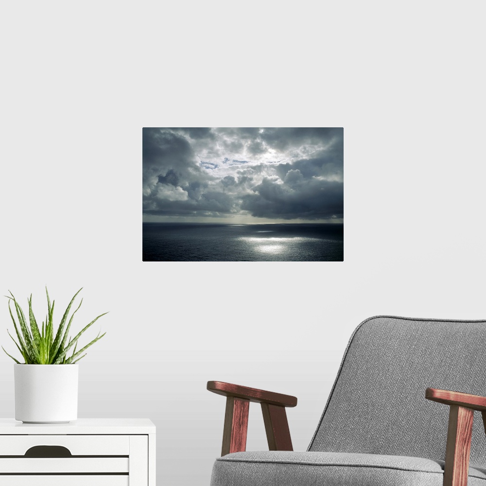 A modern room featuring Beautiful clouds formations hover over tranquil water with sunlight reflections and a storm in th...