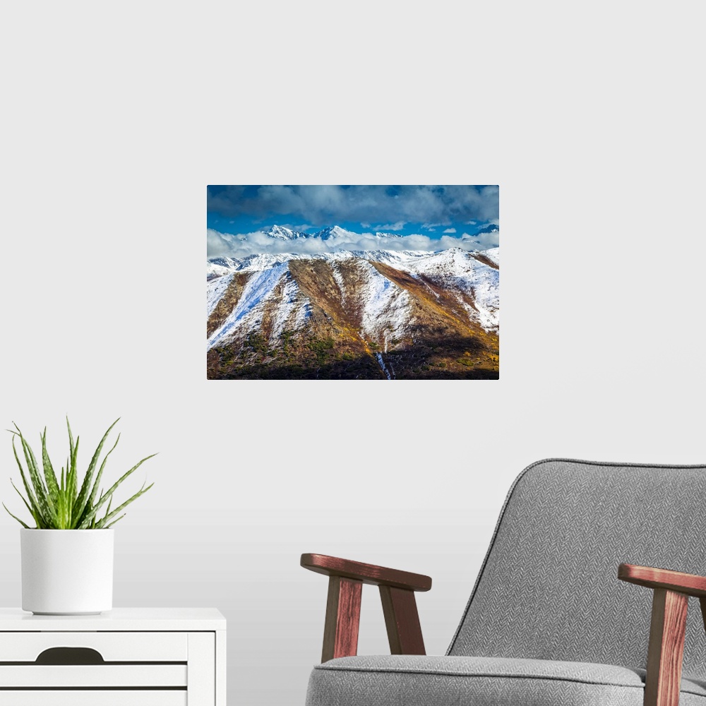 A modern room featuring Fall coloured Chugach Mountains dusted with snow, jagged peaks in the background. Chugach State P...