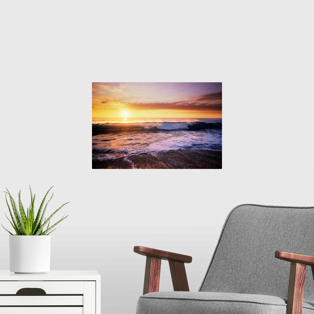 A modern room featuring The sun is setting in the distance over the ocean as a wave begins to crash near the edge of the ...