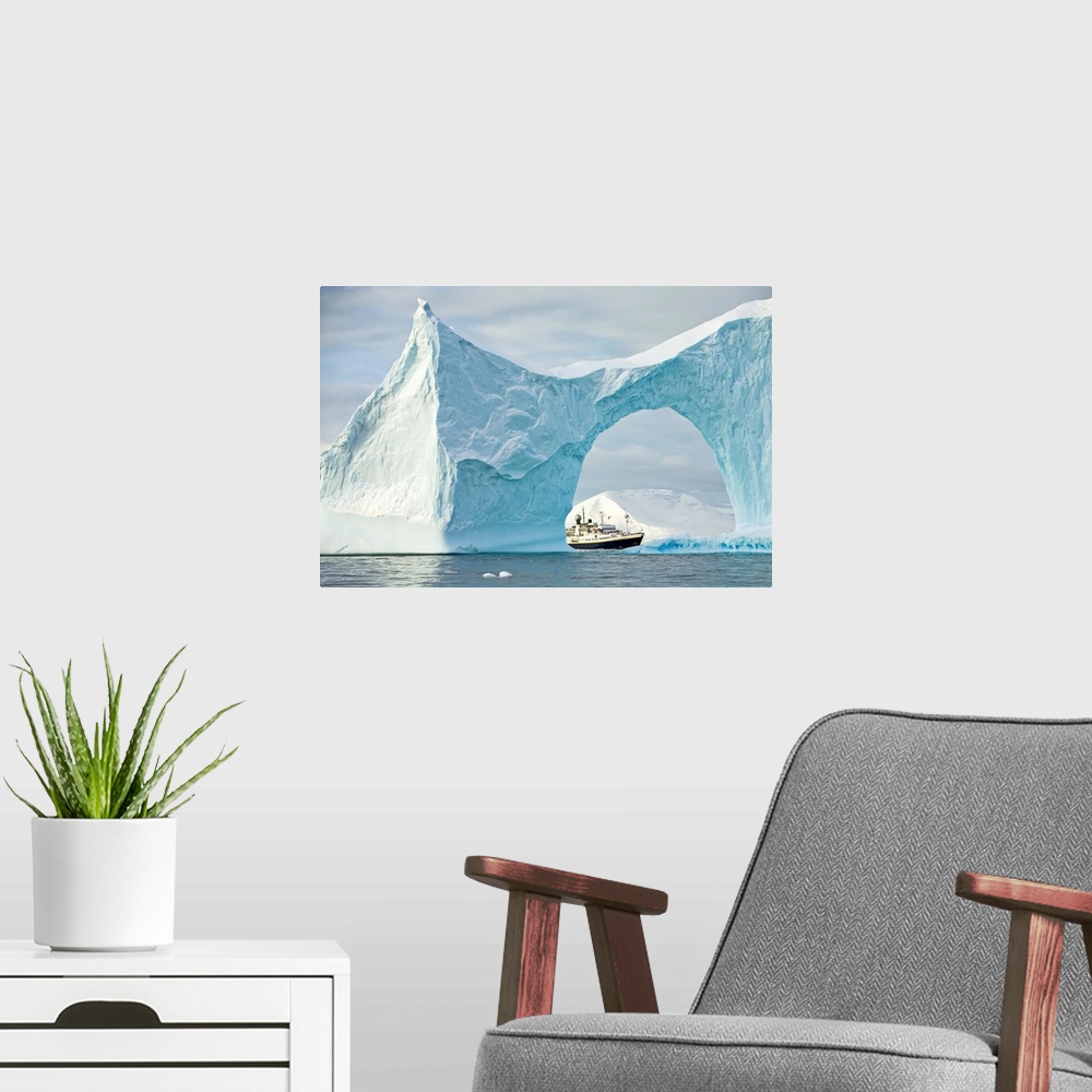 A modern room featuring Iceberg with arch frames an expedition ship in the Yalour Islands of Antarctica, Yalour Islands, ...
