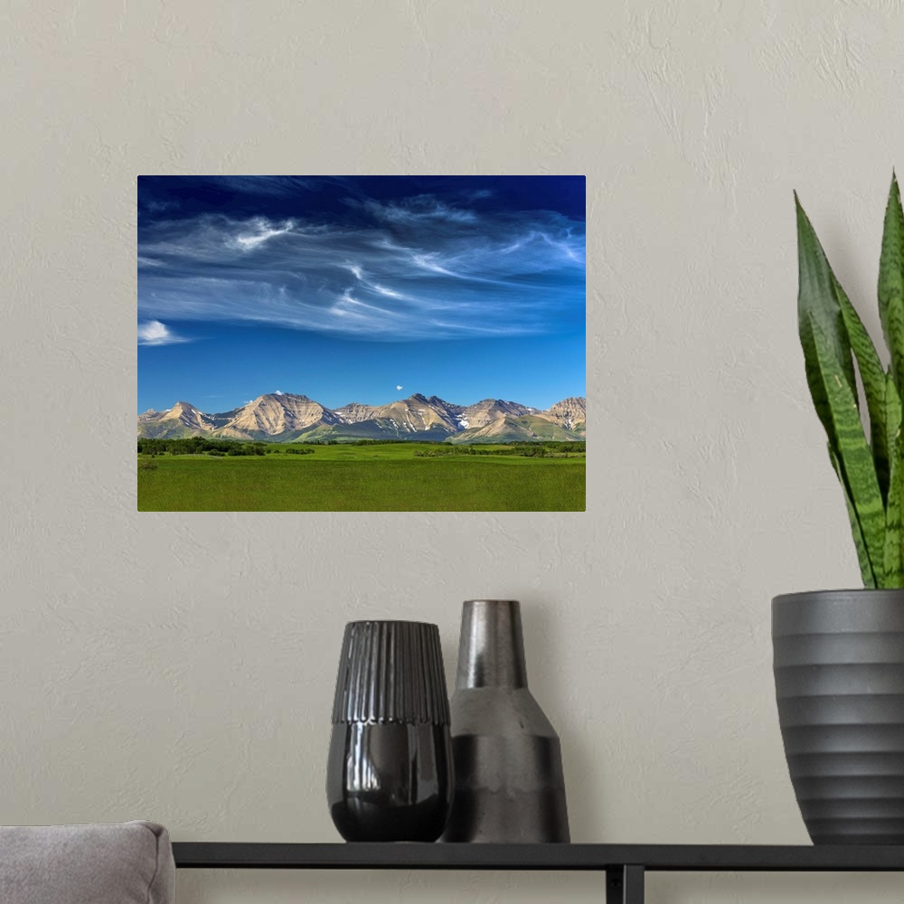 A modern room featuring Mountain range with wispy white clouds, blue sky and green field in the foreground