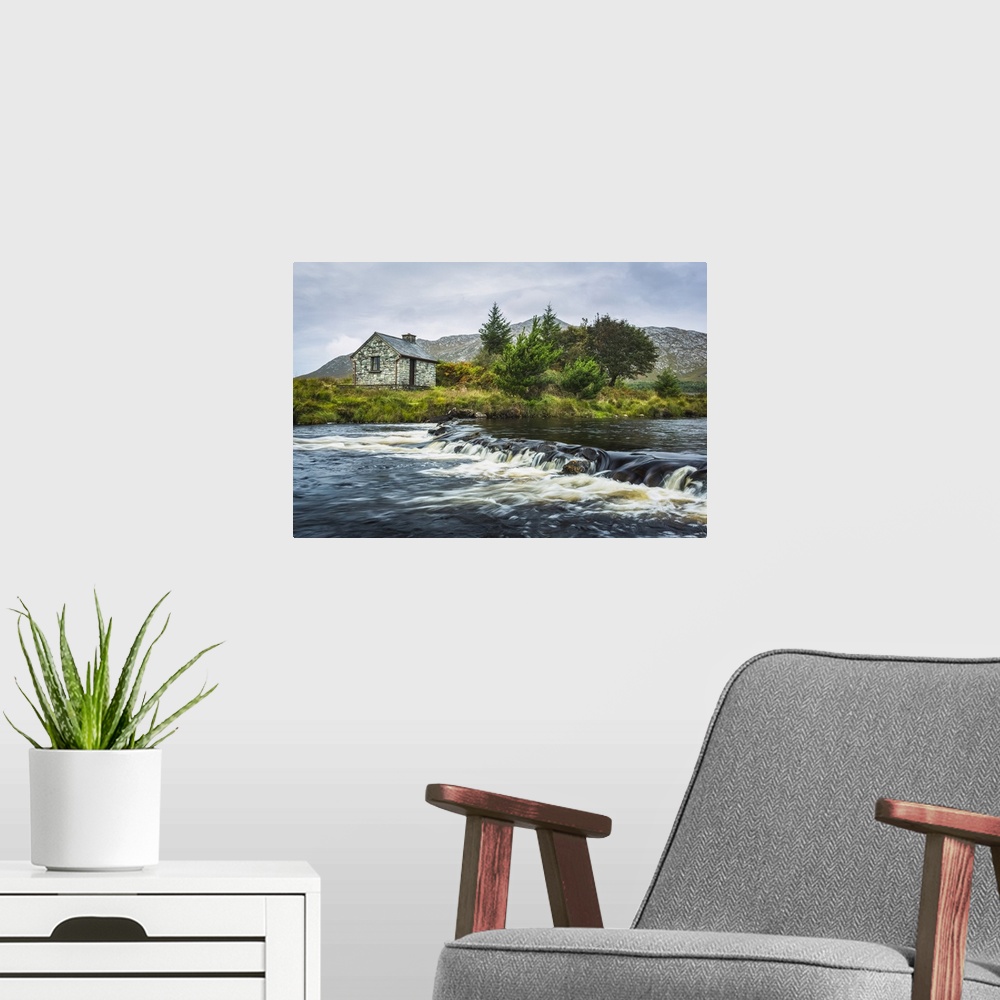 A modern room featuring Small stone fisherman's hut on the banks of a small river with mountains in the background on a c...