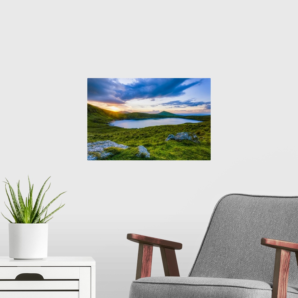 A modern room featuring Sun setting over Lough Muskery in the Galty Mountains in summer with large boulders in the foregr...