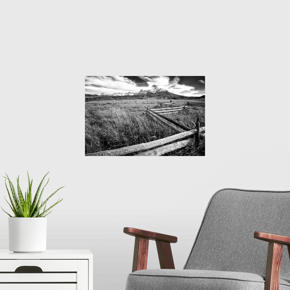 A modern room featuring Black and white landscape photograph of a field with tall grass and a wooden fence creating leadi...