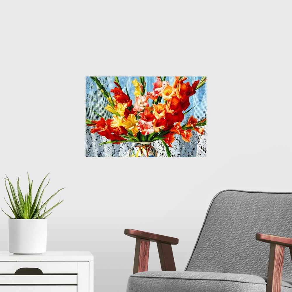A modern room featuring Contemporary vivid realistic still-life painting of bright red orange and yellow flowers in a mul...