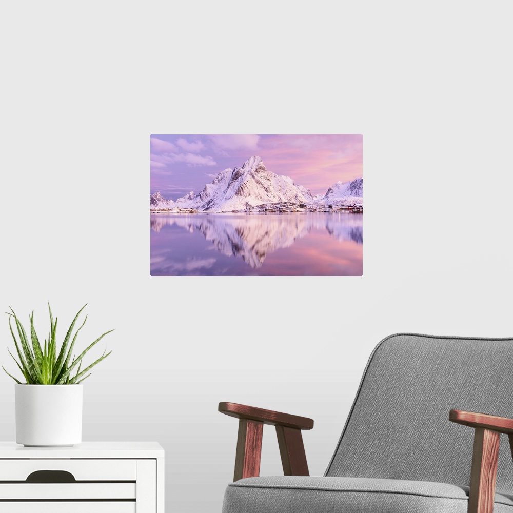 A modern room featuring A photograph of a snow covered mountain range in winter casting a clear reflection in the fjord b...