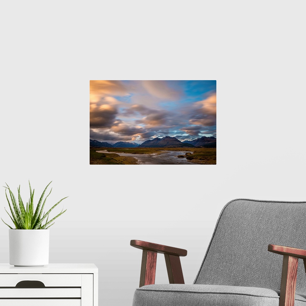 A modern room featuring Landscape photograph with a stream splitting in the middle of a field with mountains in the backg...