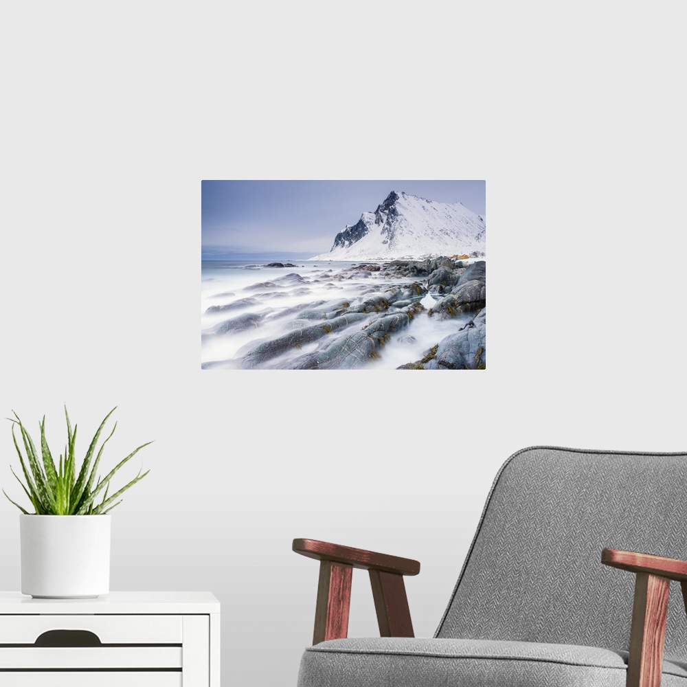 A modern room featuring A photograph of a snow covered mountain seen from a rocky shoreline with motion blurred water cau...
