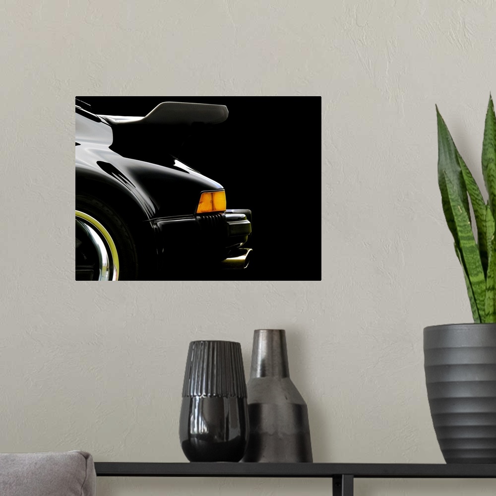 A modern room featuring Photograph of the rear and back wing of a black 78 Porsche 930 with a solid black background.