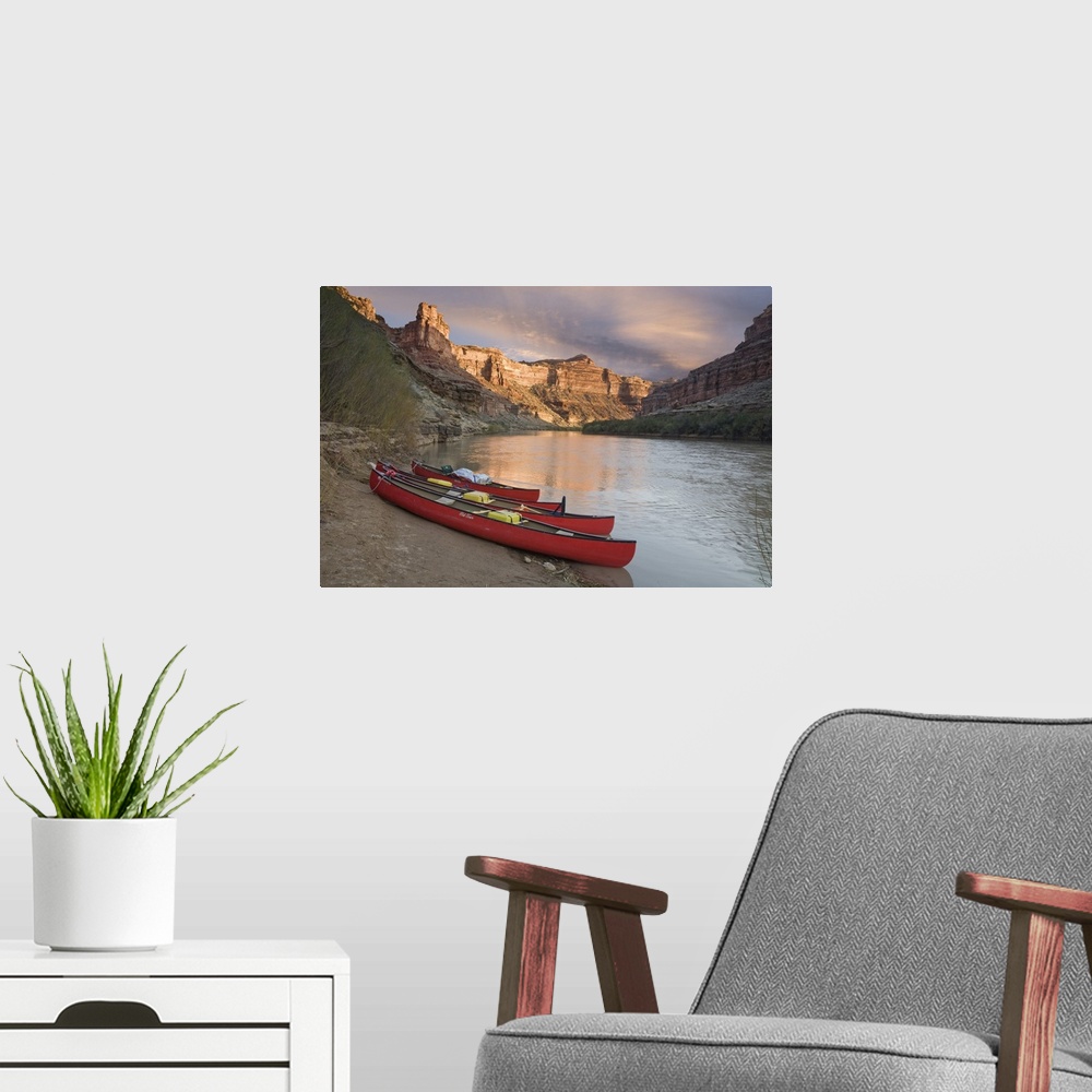 A modern room featuring USA, Utah, Canyonlands National Park. Three red canoes rest on bank of Green River.