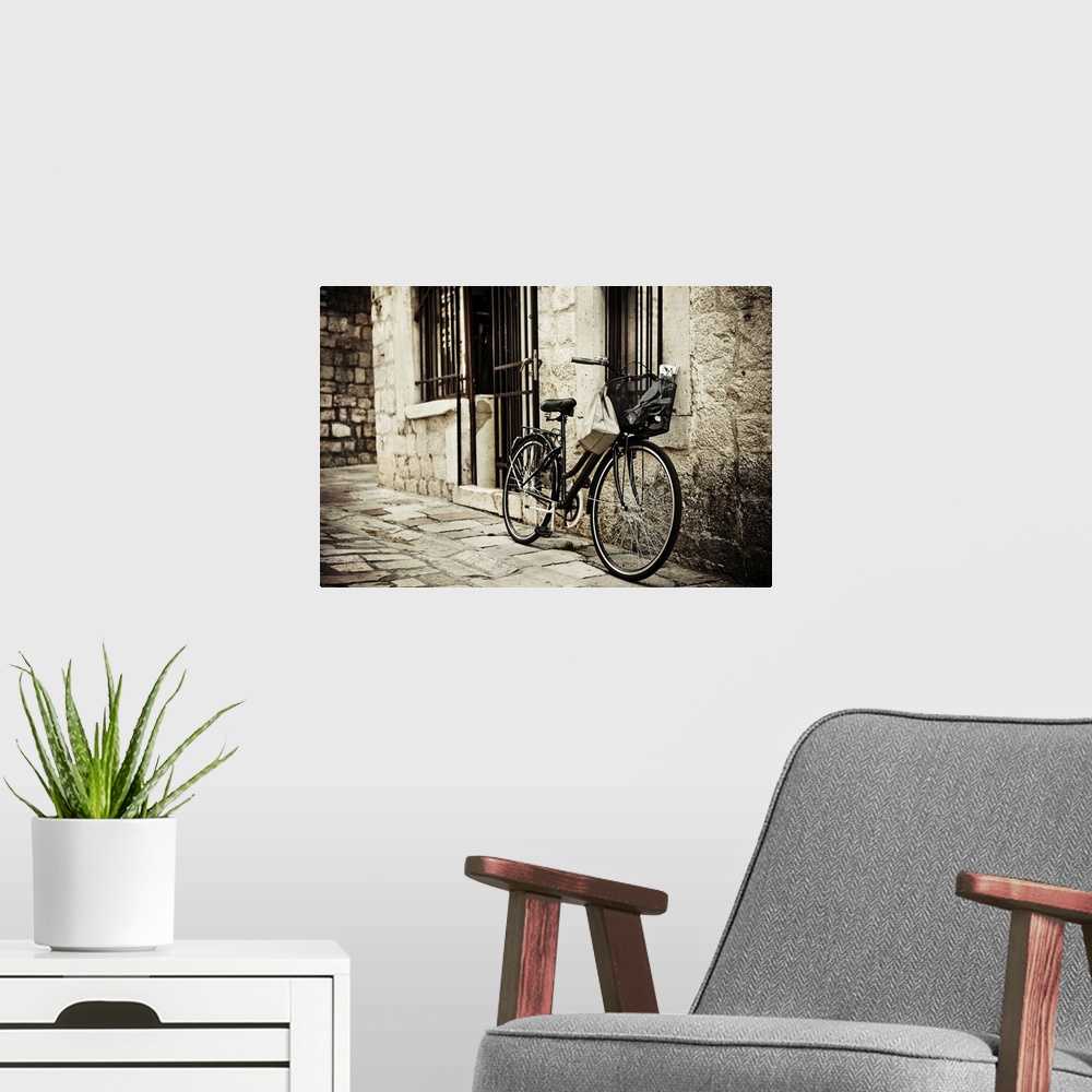A modern room featuring Old bicycle with basket and shopping bag parked in the narrow cobble street.