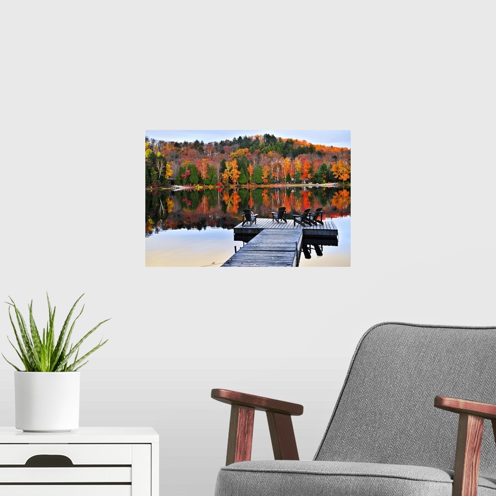 A modern room featuring Wooden dock with chairs on calm fall lake.