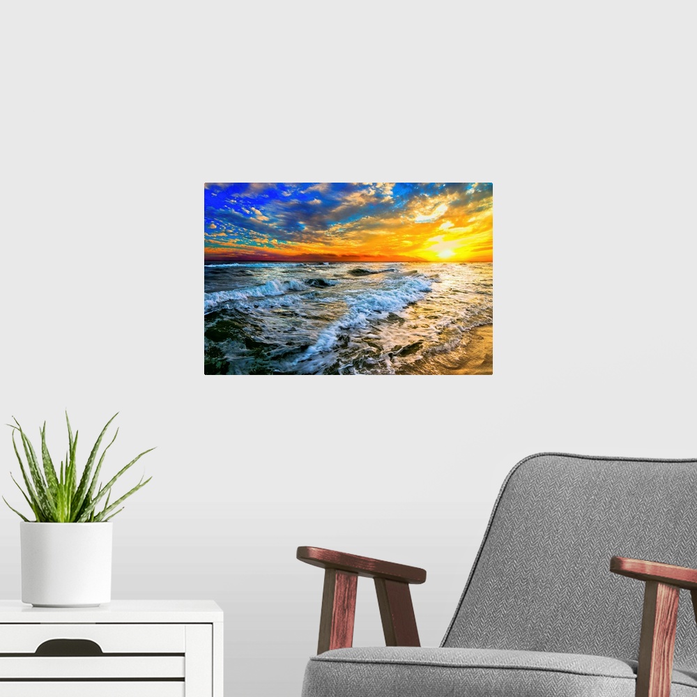 A modern room featuring Beautiful ocean waves roll in front of a yellow orange and blue sunset. The sunset goes down into...
