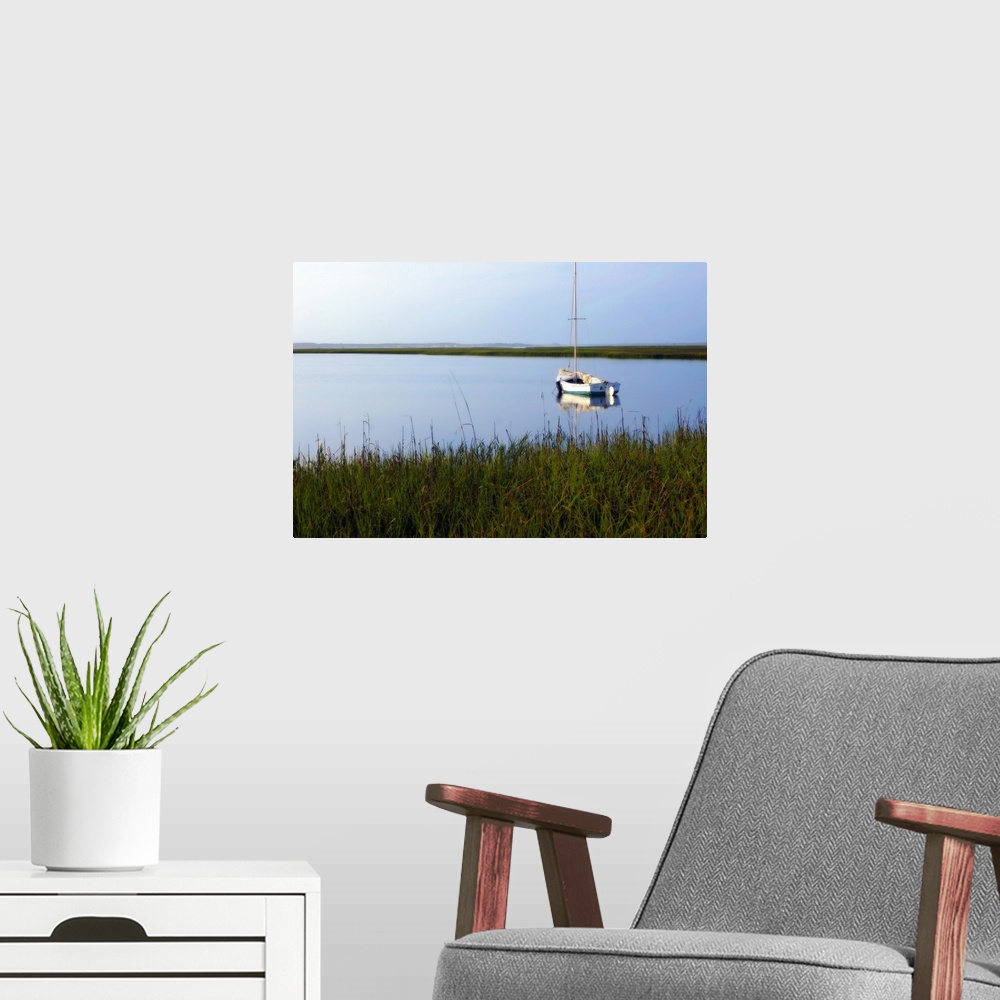 A modern room featuring A landscape photograph of a sailboat anchored in still waters surrounded by marshy grasses on the...