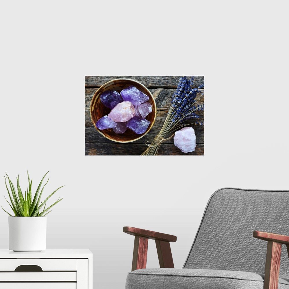 A modern room featuring A table top image of a pottery bowl with large rose quartz and amethyst crystal with dried lavend...