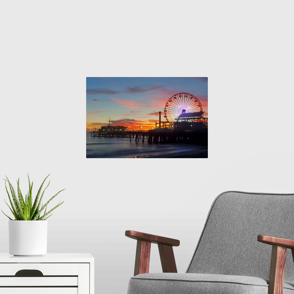 A modern room featuring Large artwork of a beach pier during sunset skies with the rides lit up and ocean waves calmly cr...