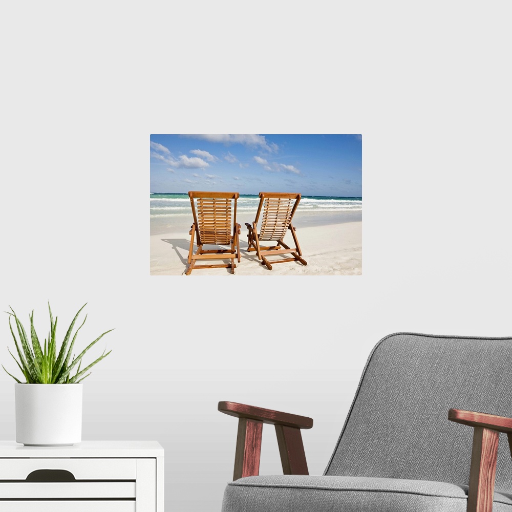 A modern room featuring Large landscape photograph of two wooden lounge chairs sitting on the beach, beneath a blue sky.