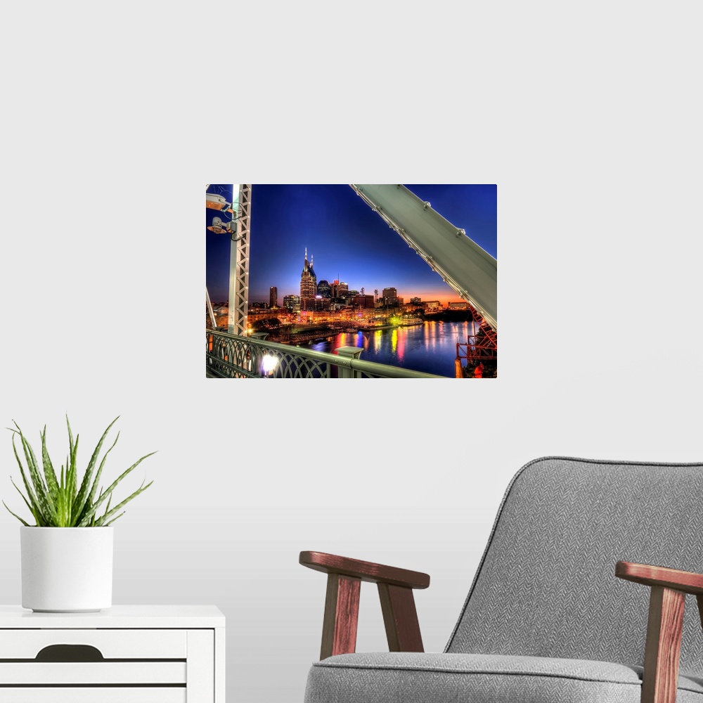 A modern room featuring Large wall docor overlooking a lit up downtown cityscape from a bridge at dusk with a river runni...