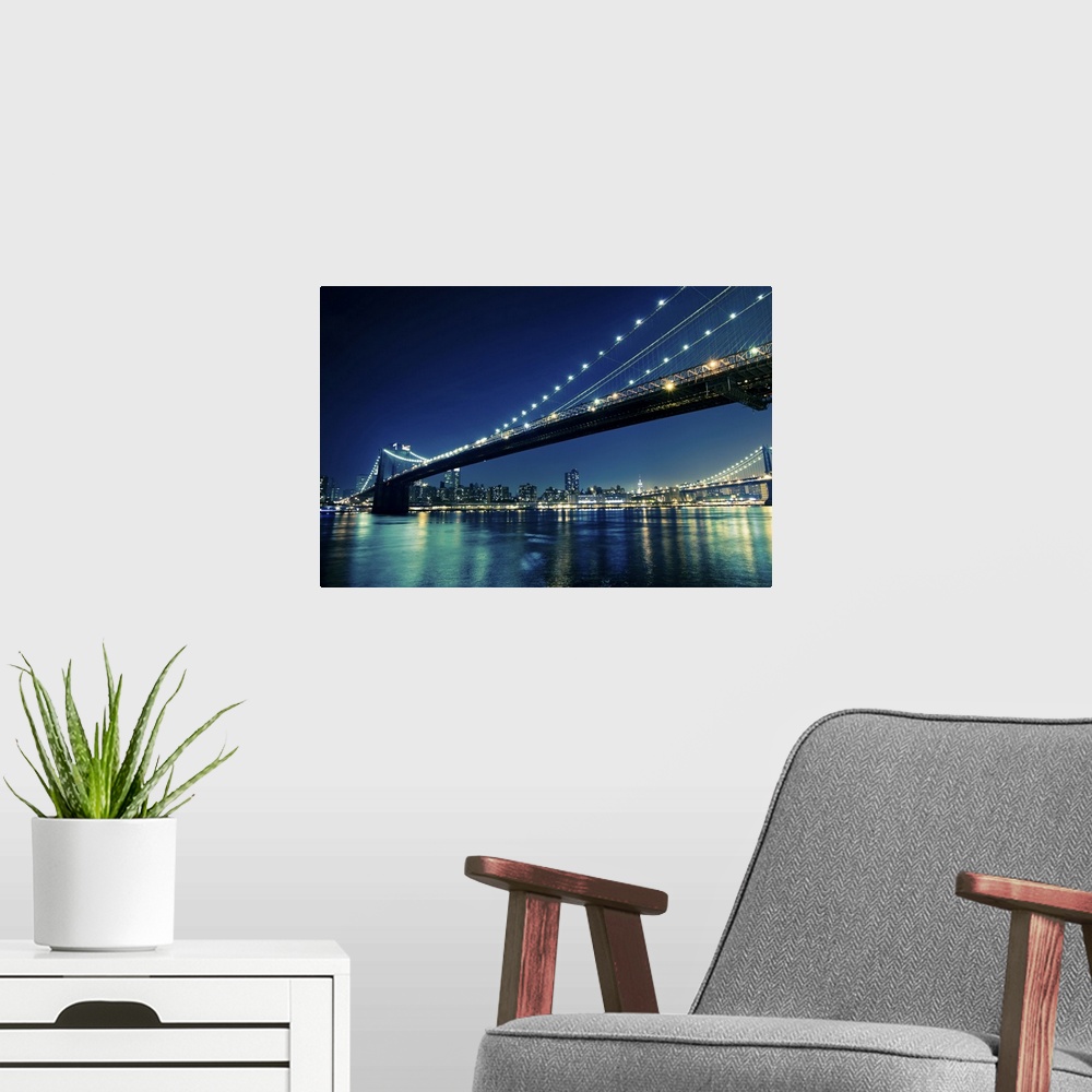 A modern room featuring The city of New York and bridges that stretch across the river are illuminated under a night sky ...