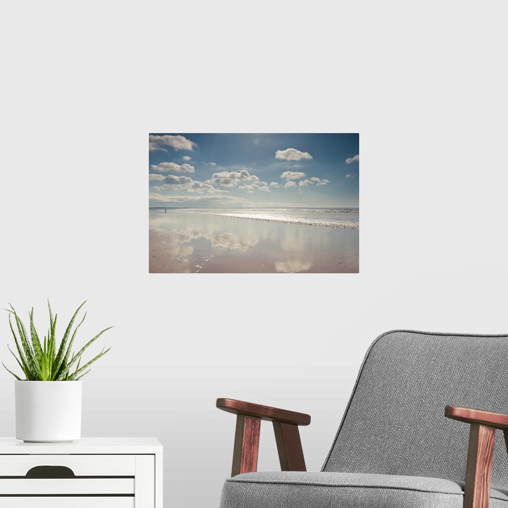 A modern room featuring Empty beach with a thin film of water reflecting fluffy clouds in a sunny blue sky.
