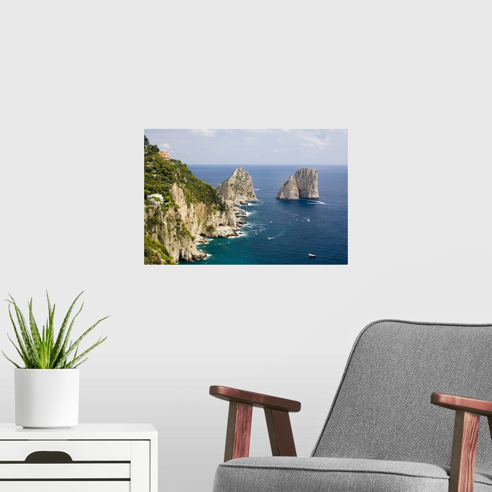 A modern room featuring Large rock formations stand in the water next to an immense cliff off the Italian coast.