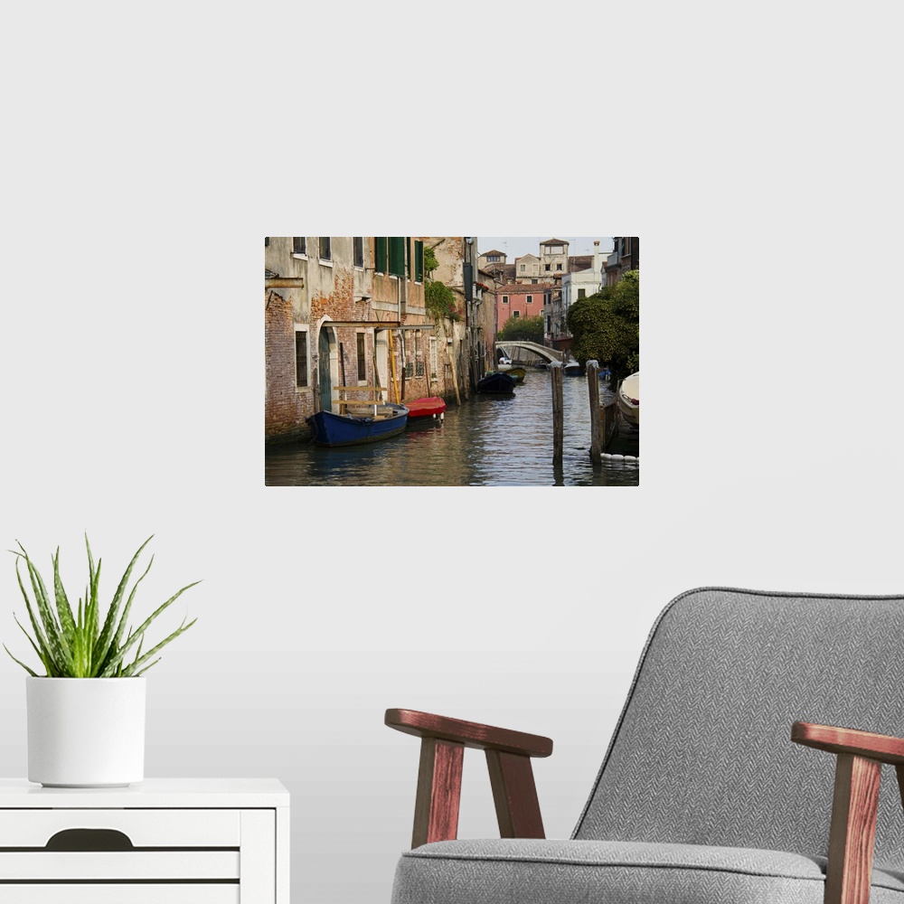 A modern room featuring A picture of a canal is taken with boats docked on the left side where buildings line the water.