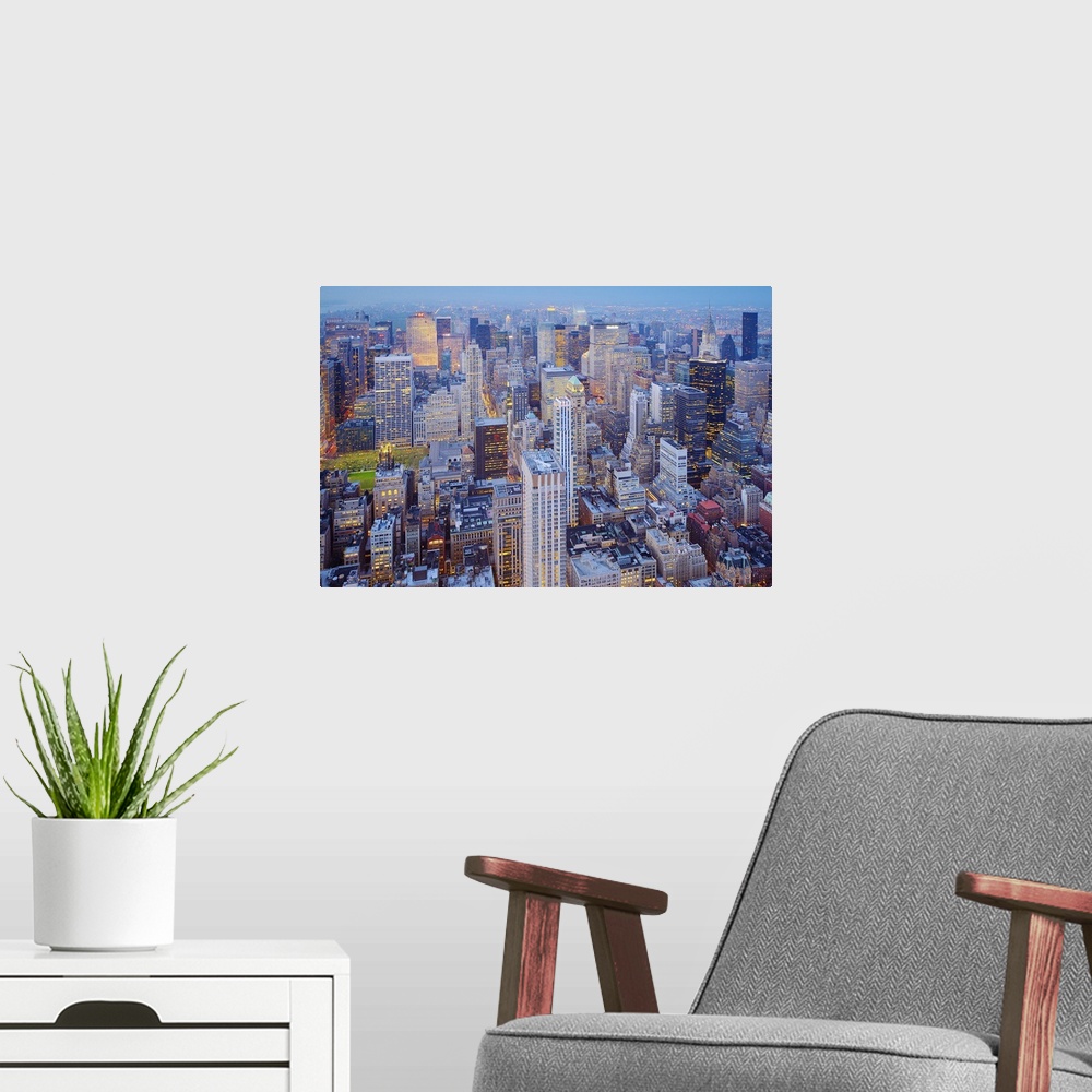 A modern room featuring An aerial view of immense skyscrapers in the New York City skyline at night with the windows illu...