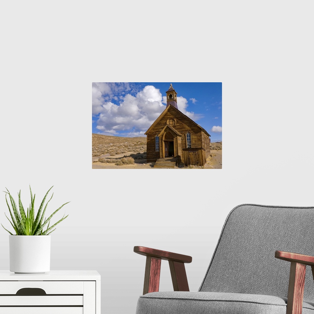 A modern room featuring Large, horizontal photograph of a small, old wooden church surrounded by empty dessert, beneath a...