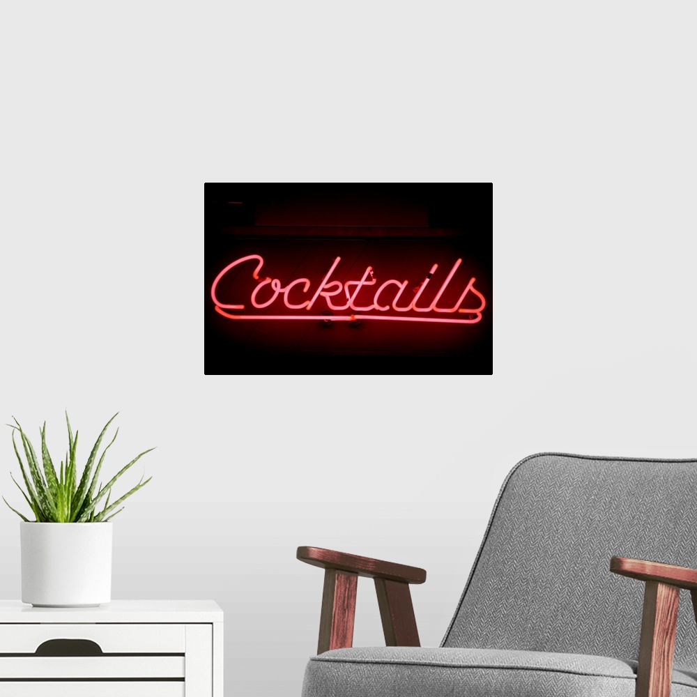 A modern room featuring An illuminated pink sign with the work cocktails sits on a dark wall.