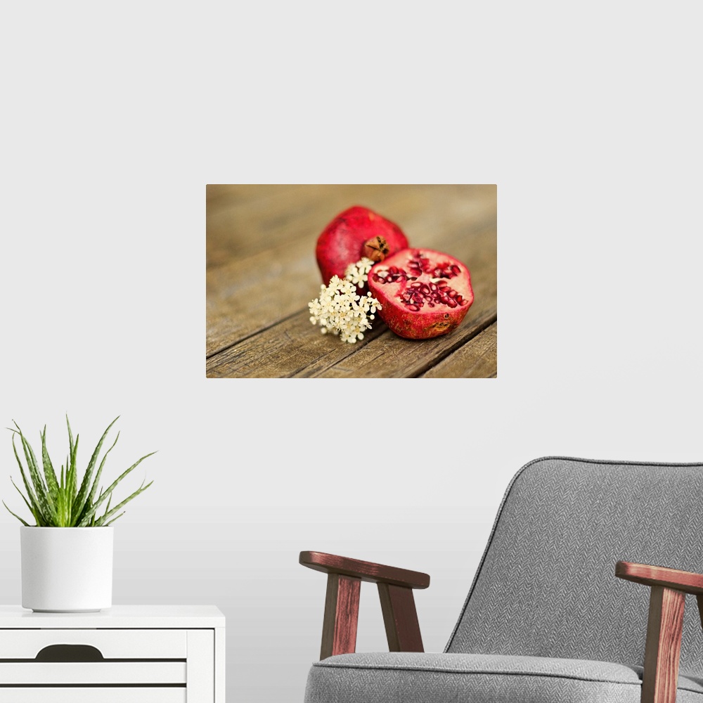 A modern room featuring Pomegranate fruit cut in half, with cluster of tiny white flowers on rustic looking wooden tabletop.