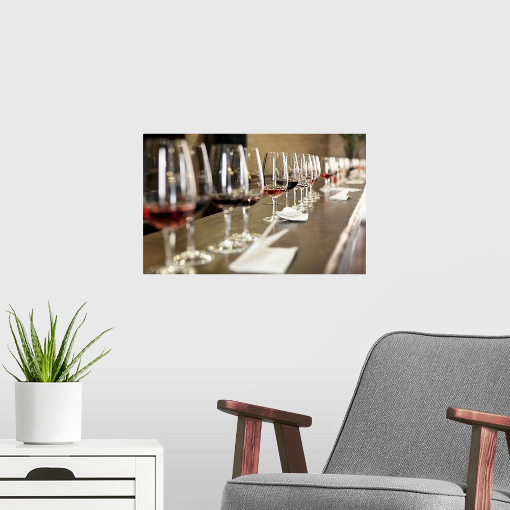 A modern room featuring A long row of wine glasses set up so a large group of people can taste wines