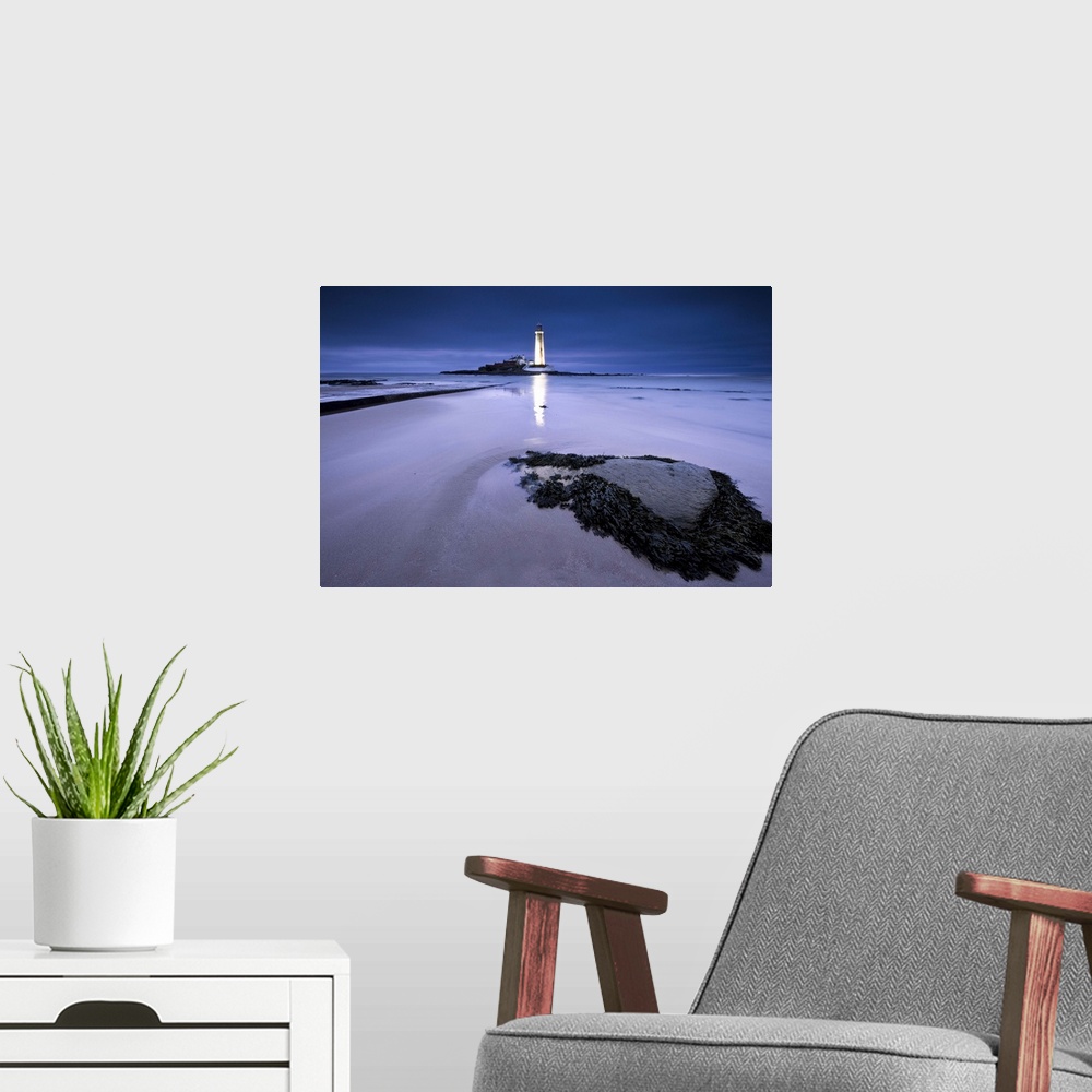 A modern room featuring St.Marys Lighthouse, Whitley Bay, glowing at night in blue hour, reflected on sand in front of se...