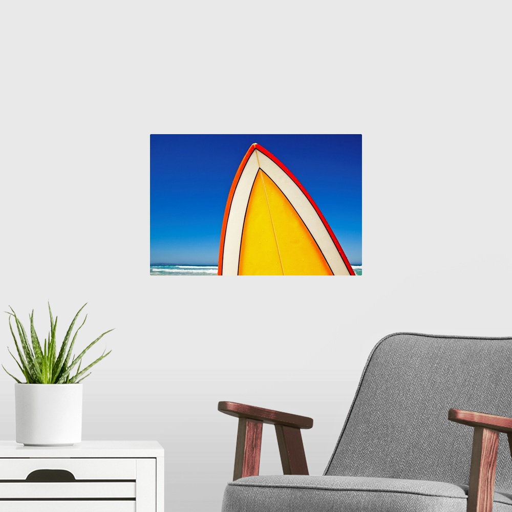 A modern room featuring The very top of a surfboard is photographed with a view of the deep blue sky and ocean just behin...